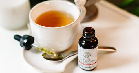 Frasco de aceite de CBD con gotero junto a una taza de té