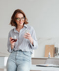 Mujer en cocina con su telefono junto a un frasco de tintura de CBD CBD Life