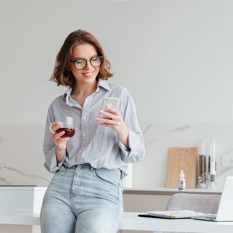 Mujer en cocina con su telefono junto a un frasco de tintura de CBD CBD Life